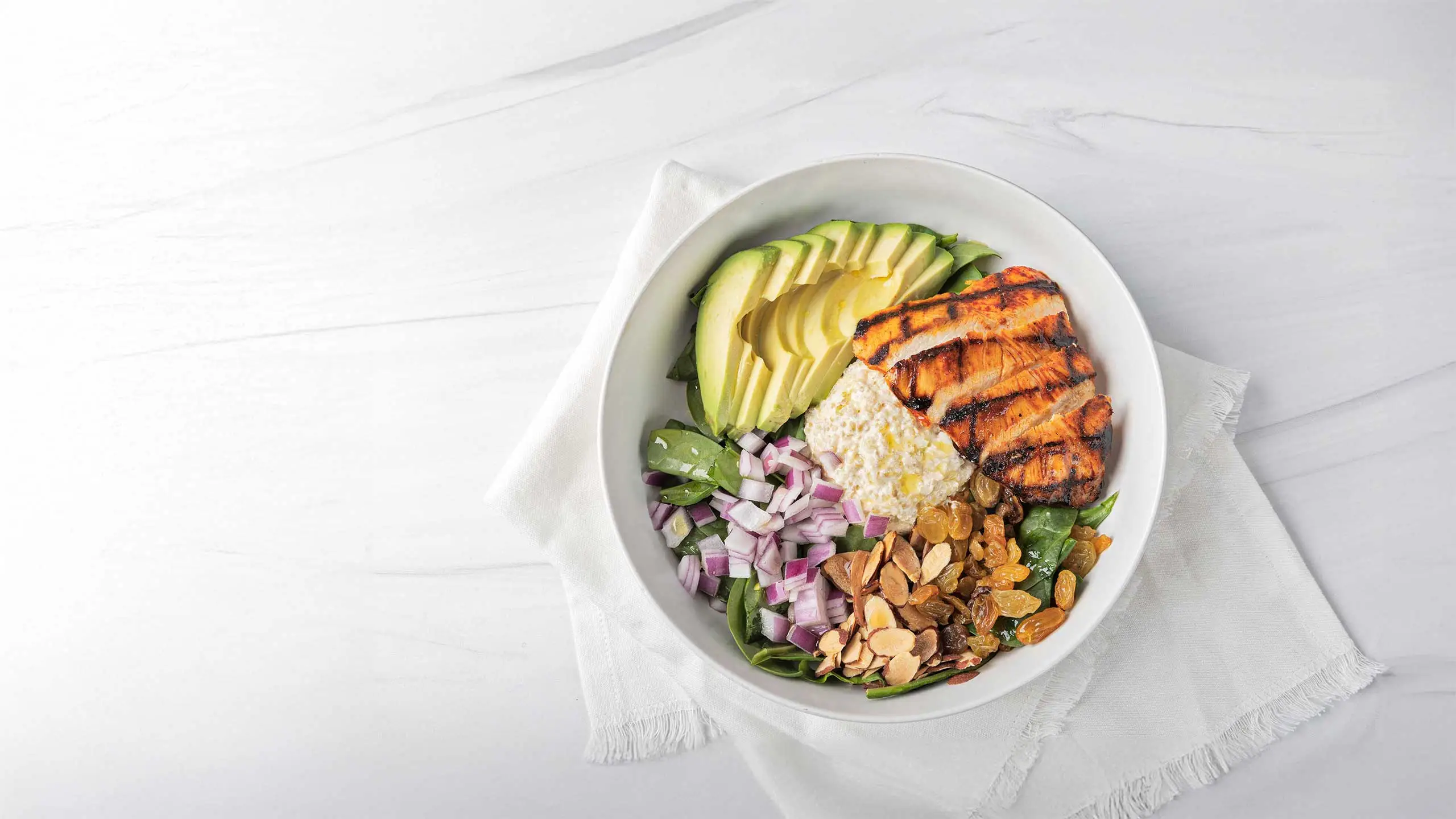 An overhead shot of grilled chicken and hummus salad bowl
